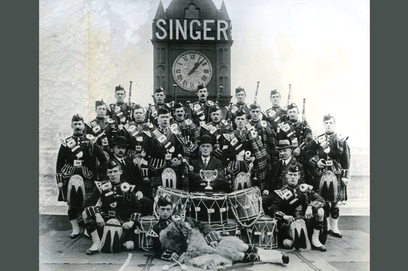 image of Singer Manufacturing Company Pipe band in front of Singer clock in 1920.