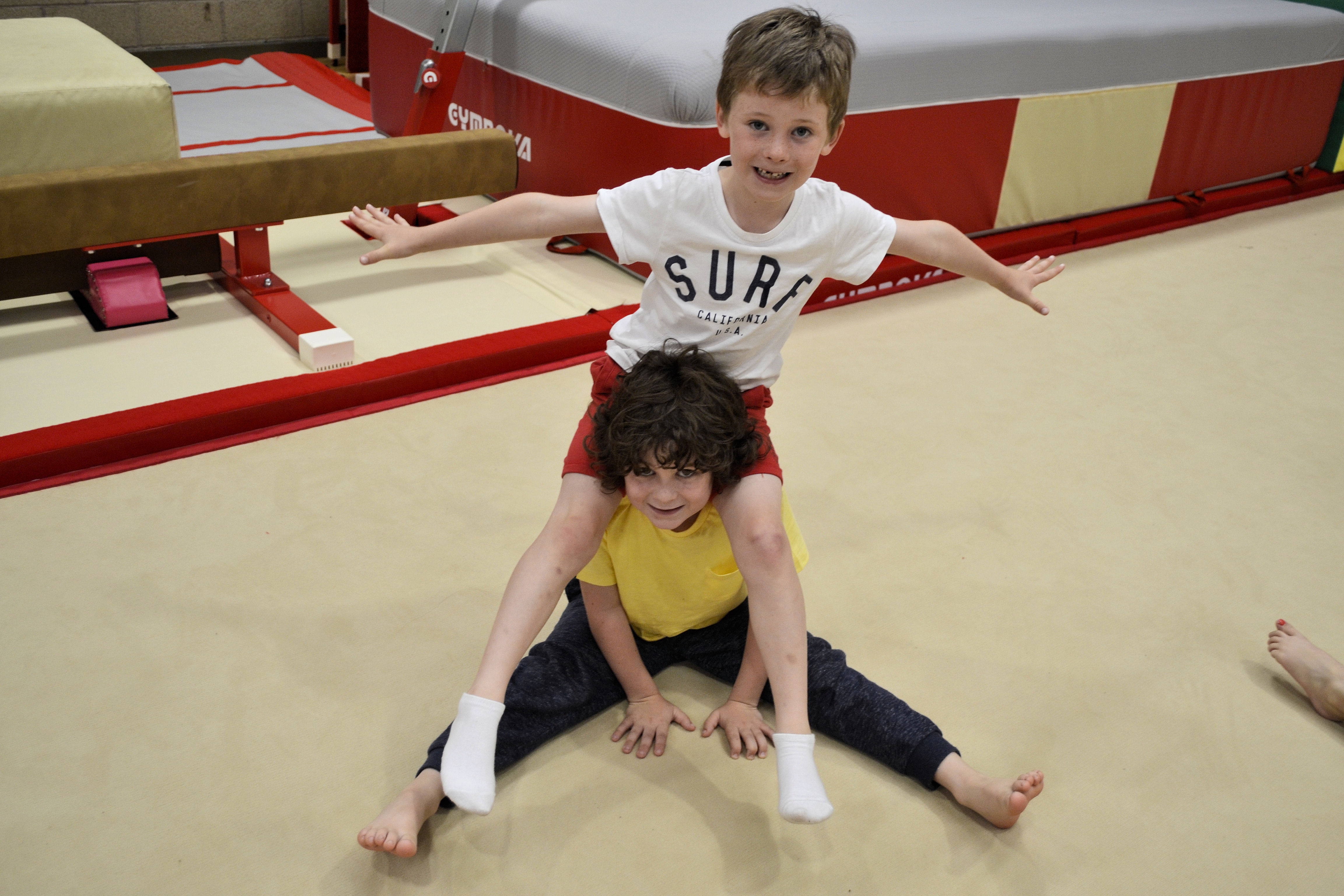 image of Gymnastics - boy sitting with another boy on his shoulders with arms out