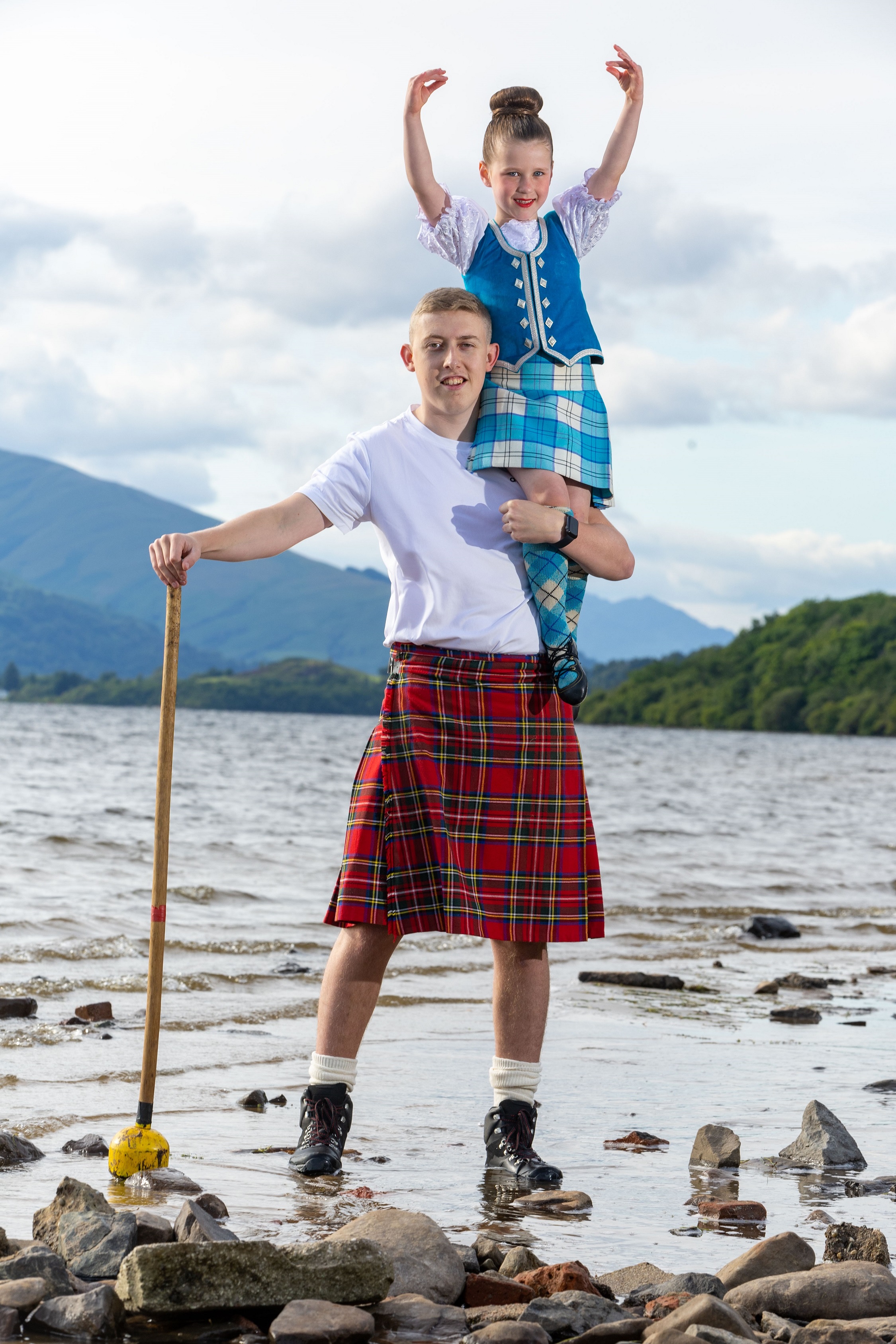 Young highland dancer on man in kilt shoulders at Loch Lomond
